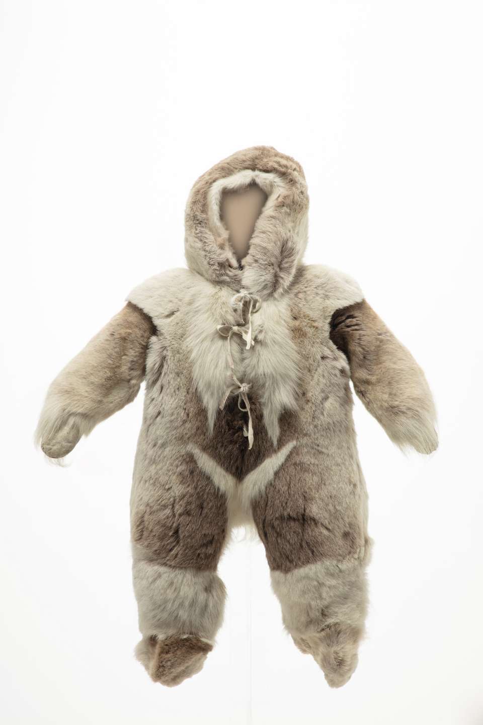 Combinaison en fourrure, vue de face, avec un capuchon ajust&eacute;, des mitaines et des bottes int&eacute;gr&eacute;es. La fourrure est de couleur brune avec des variations plus claires au niveau de l&rsquo;abdomen et des jambes, et plus fonc&eacute;es au milieu du dos et au niveau des bras. La combinaison est ferm&eacute;e par un lacet &agrave; l&rsquo;avant au niveau de la poitrine et du cou.