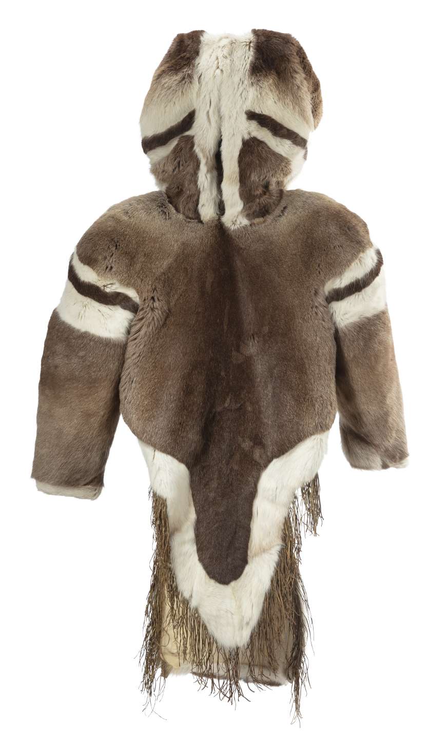 Manteau en fourrure brune, vu de face, avec le capuchon relev&eacute;. Des bandes de fourrure claires et fonc&eacute;es sont visibles sur les &eacute;paules et les c&ocirc;t&eacute;s du capuchon. Le pan avant du manteau, plus court et arrondi que l&rsquo;arri&egrave;re, est bord&eacute; de fourrure blanche et orn&eacute; de franges.