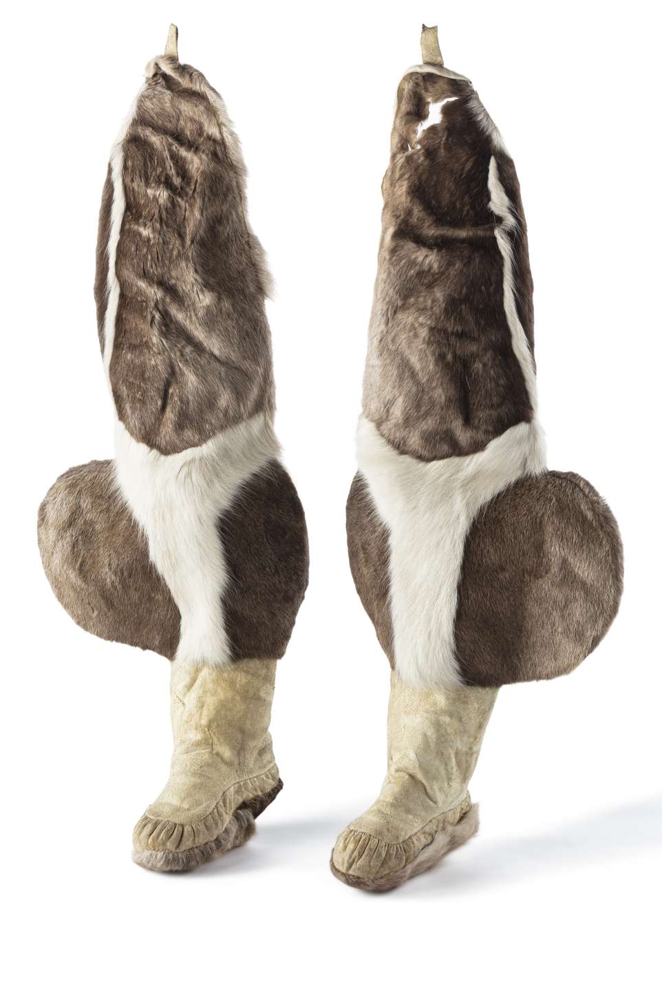 Deux bottes-jambi&egrave;res en fourrure, positionn&eacute;es debout l&rsquo;une &agrave; c&ocirc;t&eacute; de l&rsquo;autre. Les bottes sont surmont&eacute;es de jambi&egrave;res bouffantes, avec des poches lat&eacute;rales arrondies au niveau des mollets. Les bottes sont en cuir beige et les jambi&egrave;res sont en fourrure brune avec des motifs en fourrure blanche.