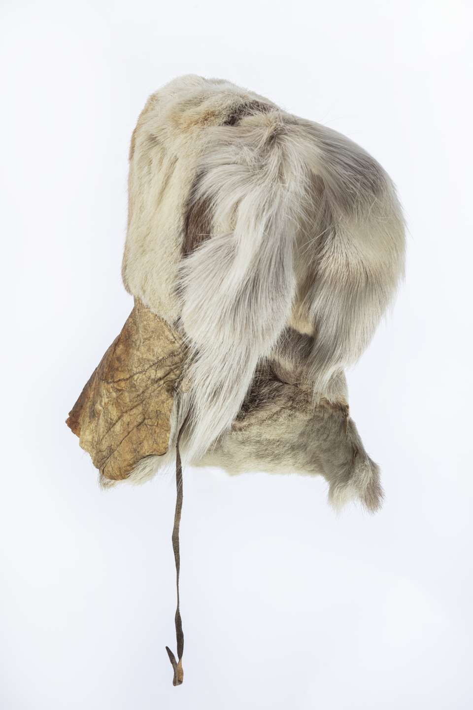 Capuchon en fourrure beige, vu lat&eacute;ralement, avec une bande de fourrure brune sur le c&ocirc;t&eacute;. La fourrure beige qui entoure l&rsquo;ouverture pour le visage est plus longue. Le capuchon a une encolure en cuir qui se termine par une lani&egrave;re fine pendante.