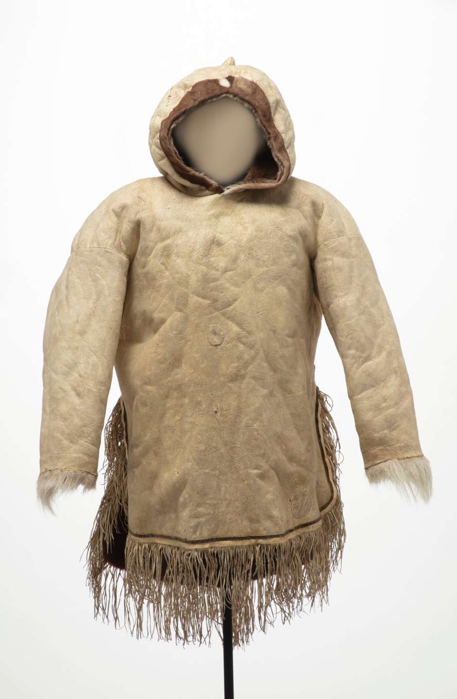 Veste en cuir beige vue de face, avec un capuchon pointu et relev&eacute;. La veste est fendue sur les c&ocirc;t&eacute;s, et d&eacute;cor&eacute;e de longues franges au bas et de fourrure blanche au niveau des poignets.