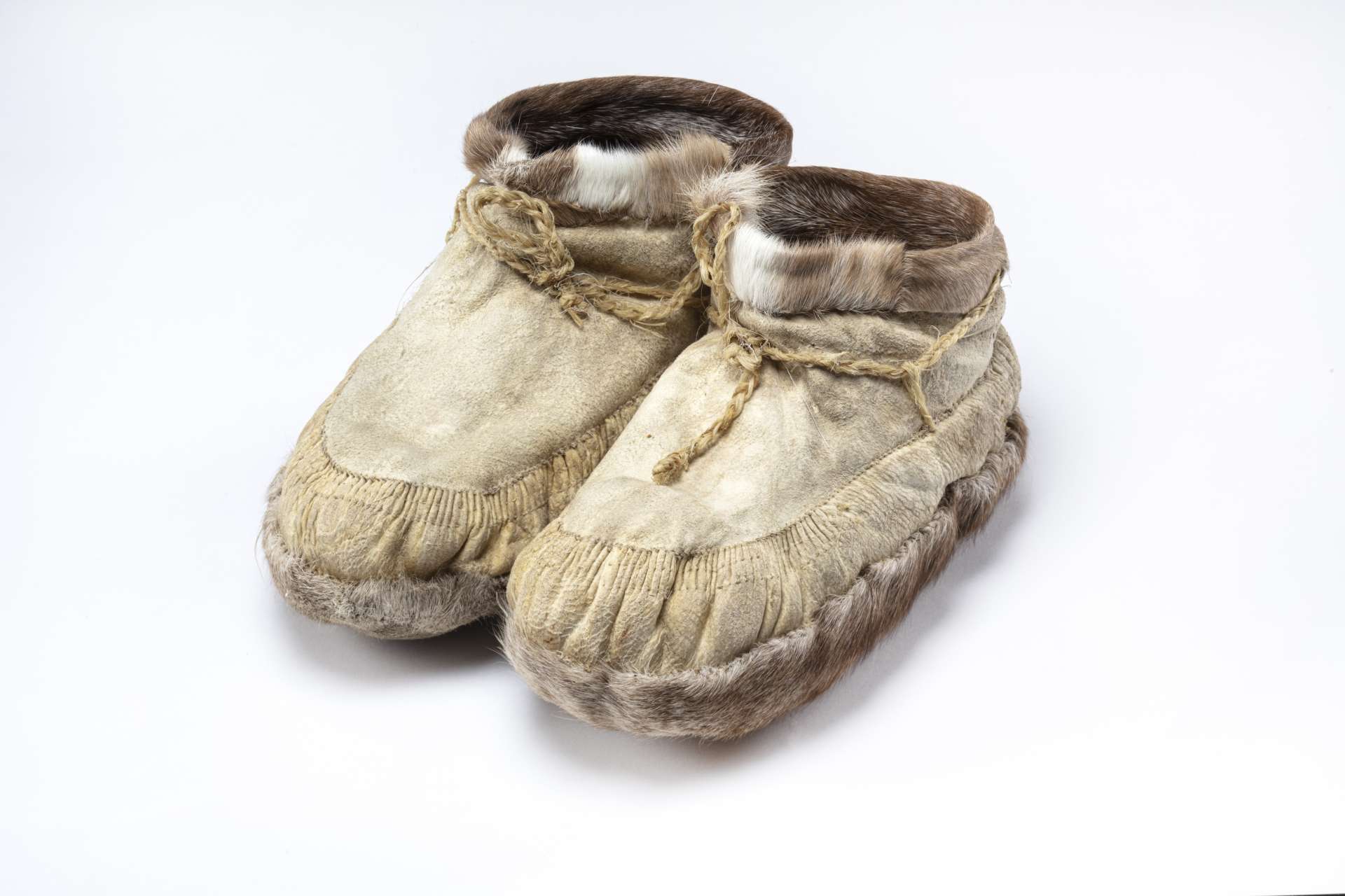 Une paire de bottillons, en cuir beige, orn&eacute;s de fourrure brune et blanche autour des chevilles, de fourrure brune sous la semelle et de cordons de serrage.