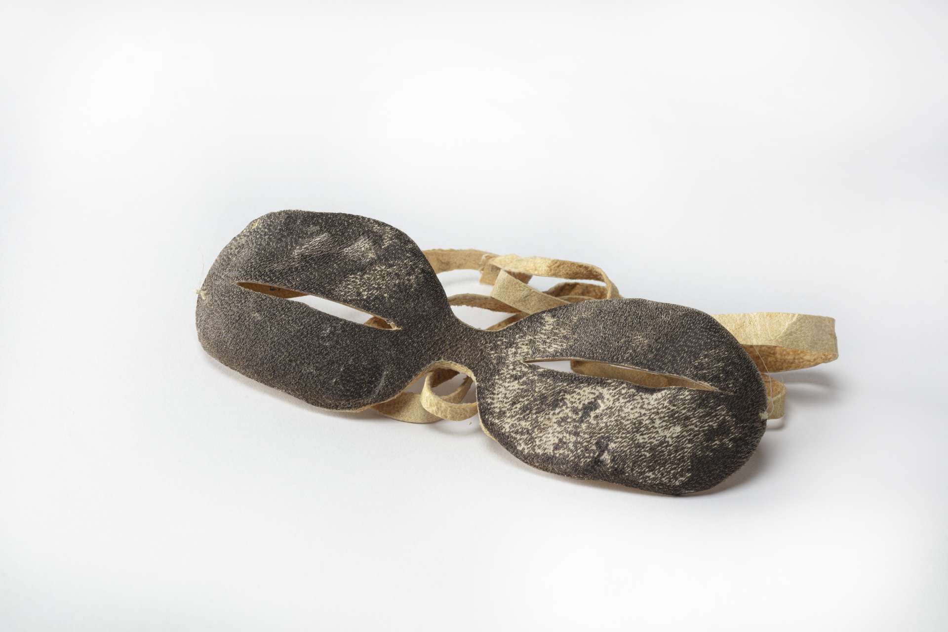 Lunettes en cuir brun fonc&eacute;, vues de face, avec deux fentes &eacute;troites pour les yeux et une sangle en peau beige.