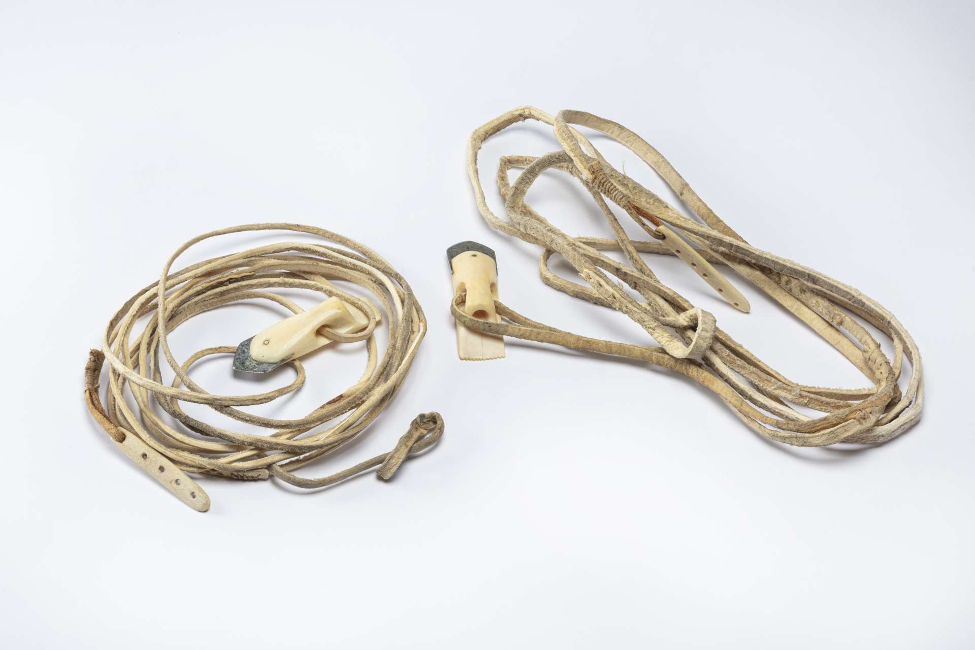 Deux longues cordes de cuir enroul&eacute;es, chacune munie d&rsquo;une t&ecirc;te de harpon en mati&egrave;re osseuse blanche et sa lame de m&eacute;tal &agrave; une extr&eacute;mit&eacute; et d&rsquo;une boucle en corde &agrave; l&rsquo;autre. Une pi&egrave;ce en ivoire &agrave; quatre trous est attach&eacute;e &agrave; chacune des cordes.