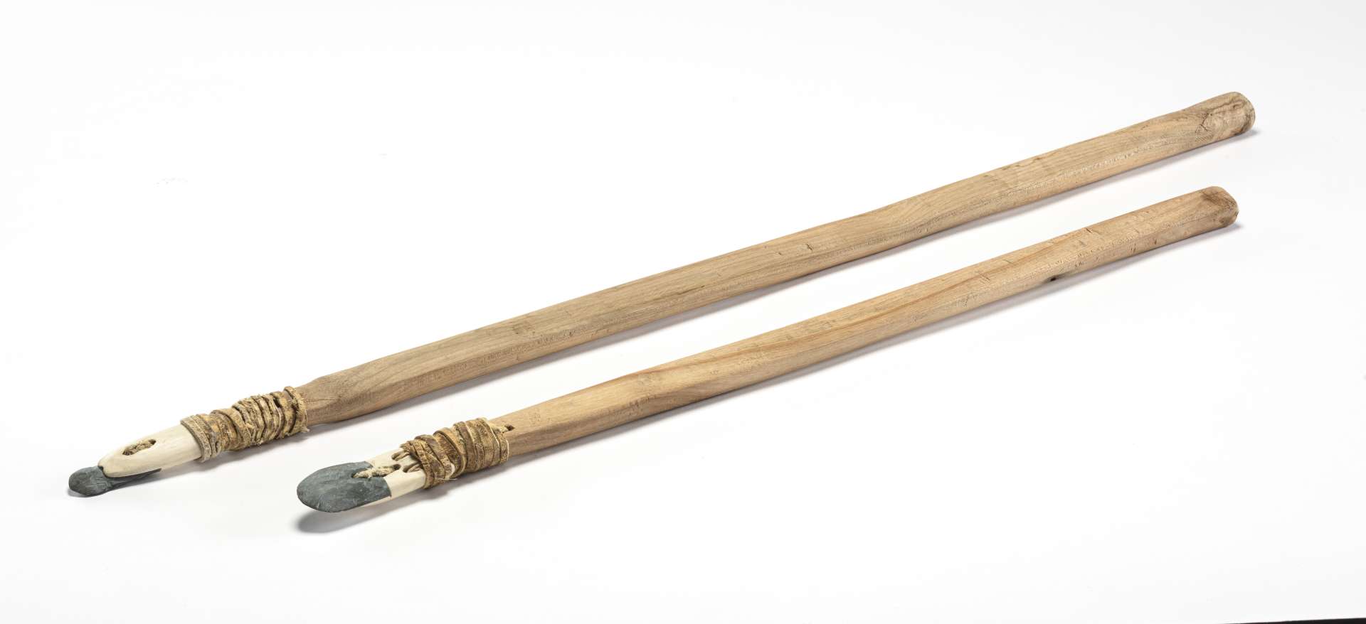 Deux ciseaux &agrave; glace compos&eacute;s d&rsquo;un long manche en bois et d&rsquo;une t&ecirc;te en mati&egrave;re osseuse blanche, chacun muni d&rsquo;une pointe taill&eacute;e en roche, sont dispos&eacute;s l&rsquo;un &agrave; c&ocirc;t&eacute; de l&rsquo;autre. L&rsquo;un des ciseaux est retourn&eacute;, exposant les d&eacute;tails de sa t&ecirc;te solidement enroul&eacute;e autour du manche avec une lani&egrave;re.