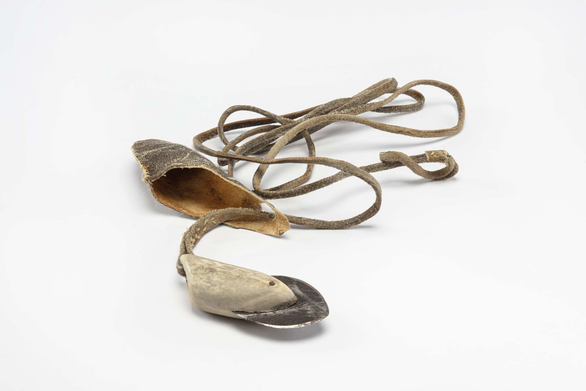 T&ecirc;te de harpon compos&eacute;e d&rsquo;une lame de m&eacute;tal ench&acirc;ss&eacute;e dans un manche en andouiller, avec un cordon en cuir. L&rsquo;ensemble est partiellement d&eacute;roul&eacute; avec un petit &eacute;tui en cuir attach&eacute; qui repose &agrave; c&ocirc;t&eacute;.