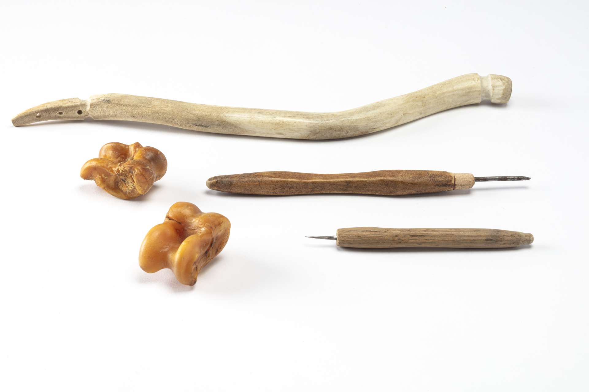 Un arc pour foret en mati&egrave;re osseuse blanche avec deux forets &agrave; manche en bois munis de pointes m&eacute;talliques et des osselets jaunis, vus de dessus. L&rsquo;arc pr&eacute;sente une forme l&eacute;g&egrave;rement incurv&eacute;e et des encoches aux deux extr&eacute;mit&eacute;s pour y maintenir une corde, manquante ici, et comporte trois petits trous align&eacute;s.