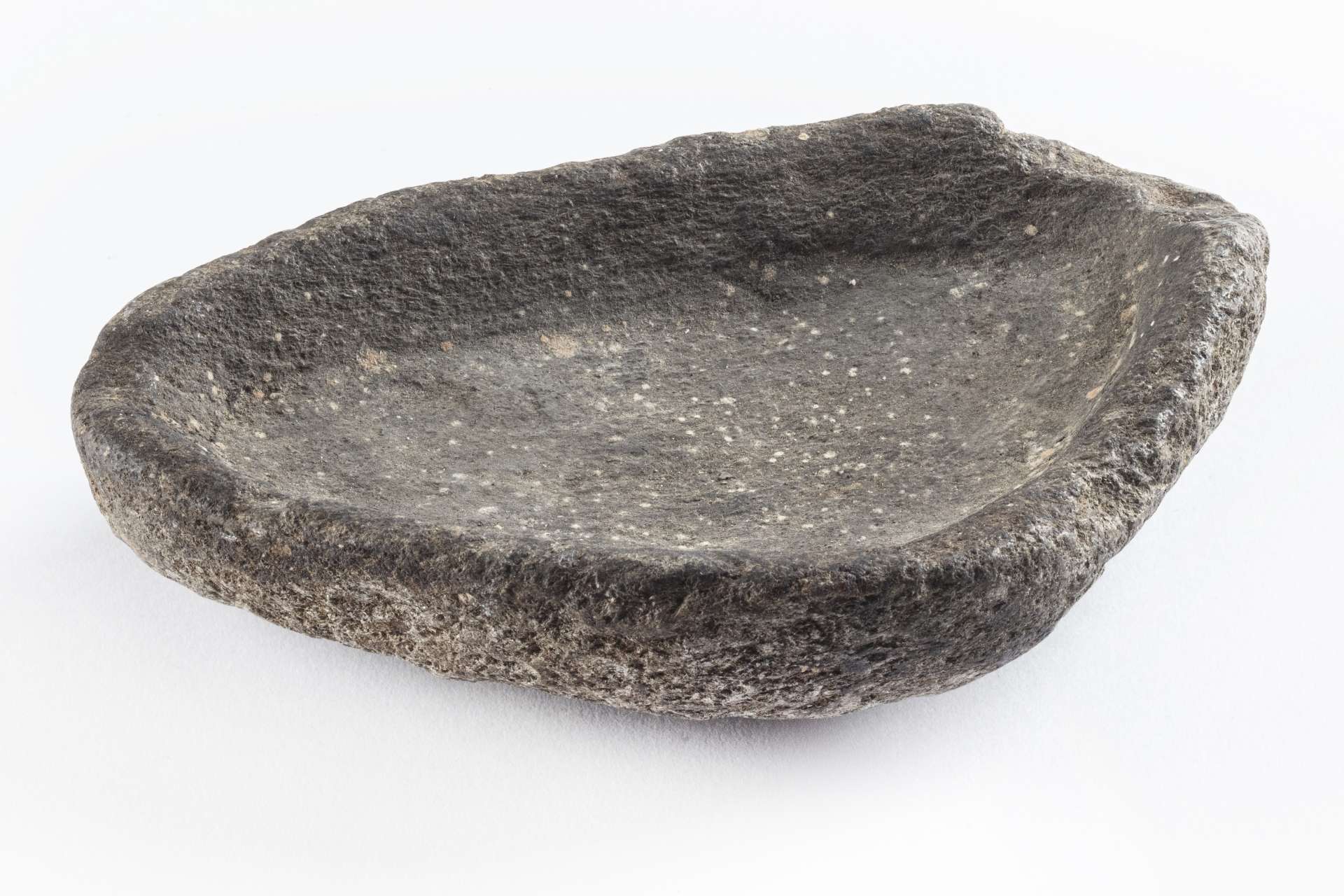 Lampe &agrave; l&rsquo;huile en roche noircie de forme demi-circulaire, mais irr&eacute;guli&egrave;re, avec un creux central. La surface de la lampe montre des traces d&rsquo;usure et des asp&eacute;rit&eacute;s.