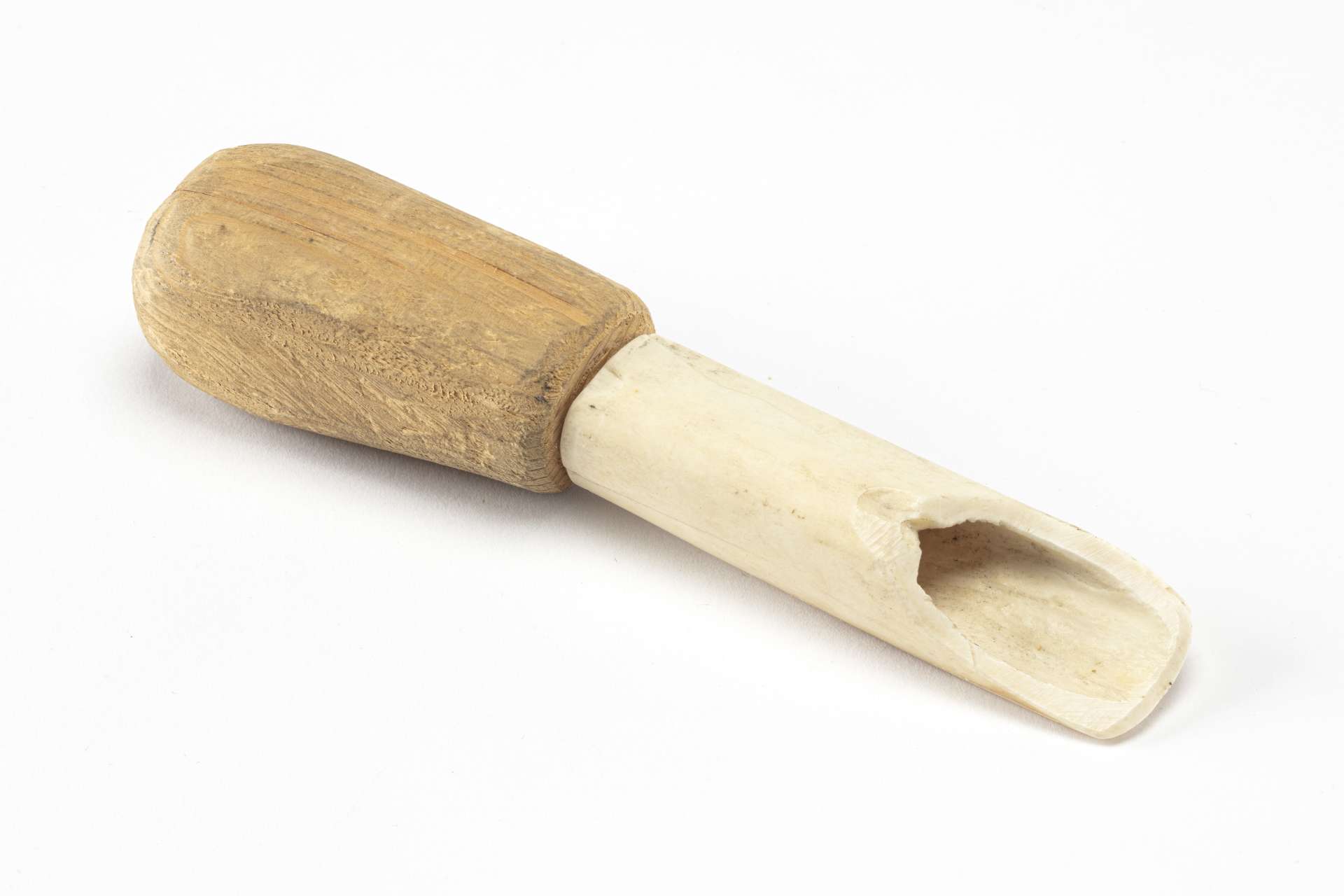 Grattoir compos&eacute; d&rsquo;un manche en bois sculpt&eacute;, de forme rectangulaire et l&eacute;g&egrave;rement arrondie sur les c&ocirc;t&eacute;s, reli&eacute; &agrave; une lame creuse taill&eacute;e dans un os blanc, pr&eacute;sentant une ouverture longitudinale &eacute;vas&eacute;e vers l&rsquo;extr&eacute;mit&eacute;.