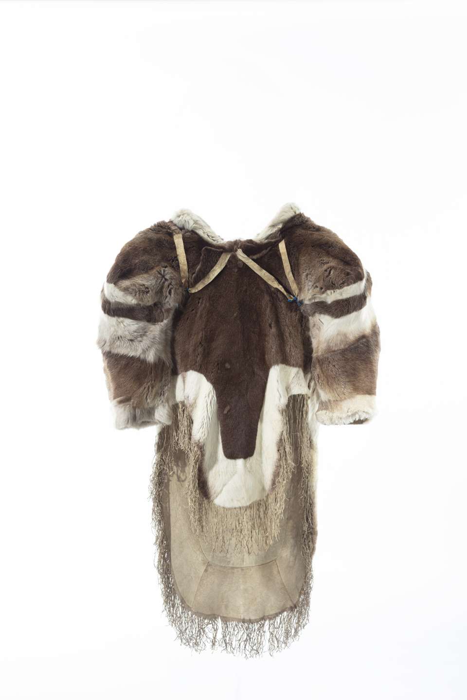 Manteau en fourrure vu en 360 degr&eacute;s, pr&eacute;sentant des &eacute;paules larges et un grand capuchon. La fourrure brune et blanche est agenc&eacute;e en bandes sur le capuchon et les &eacute;paules. Des sangles en forme de &laquo; V &raquo; sous les &eacute;paules sont visibles sur l&rsquo;avant du manteau. Le pan avant du manteau est plus court que le pan arri&egrave;re, qui sont tous deux bord&eacute;s de fourrure blanche et d&eacute;cor&eacute;s de franges au bas.