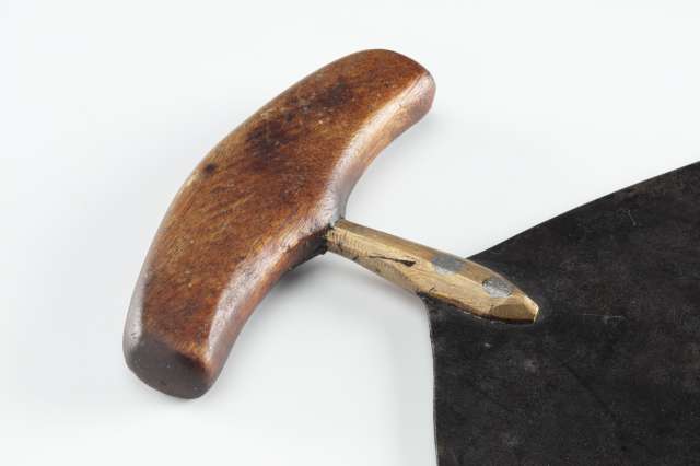 Gros plan sur le manche en bois du couteau, mettant en &eacute;vidence le support qui relie la lame au manche en bois et les rivets m&eacute;talliques qui maintiennent l&rsquo;ensemble.